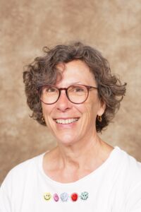 lachende Frau mit gelockten, graubraunen Haaren und brauner Brille